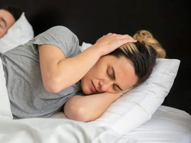 Frau im Bett und hält sich die Ohren zu