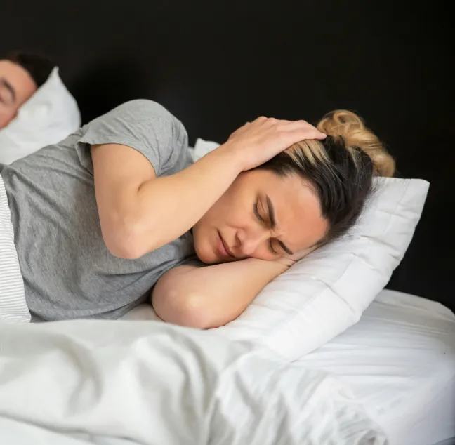Frau im Bett und hält sich die Ohren zu